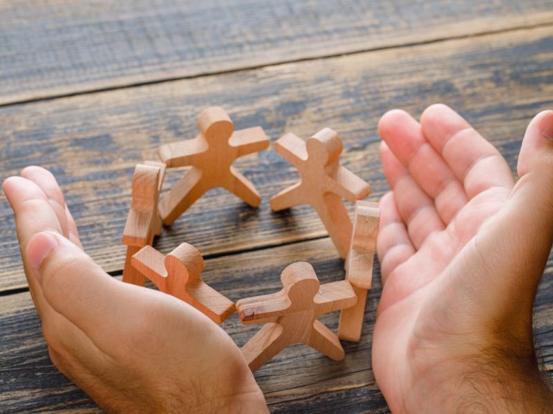 Business success concept wooden table top view hands protecting wooden figures people